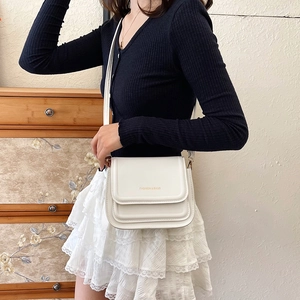 Sac bandoulière vintage blanc avec lettrage doré, porté par un mannequin en intérieur