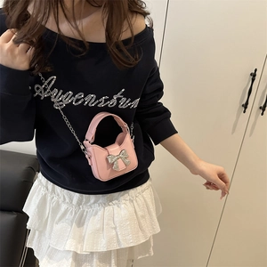 Mini sac bandoulière rose avec nœud argenté et chaîne porté par un mannequin en extérieur