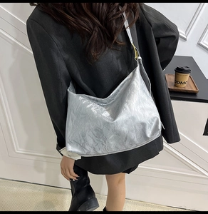 Silver tote bag with metallic crinkle finish worn by a model in a modern urban setting