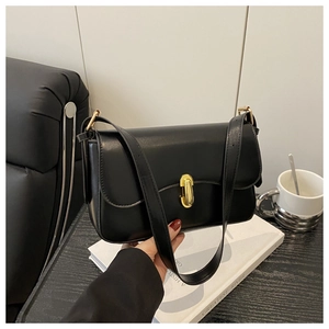 Close-up of a stylish black shoulder bag with a gold buckle held in a lifestyle setting