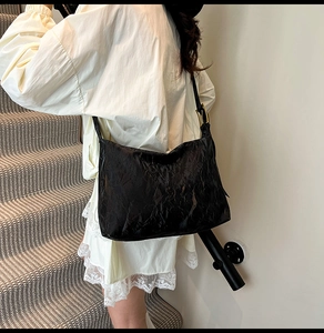 Detail of black pleated tote bag showing wrinkled texture and adjustable metal buckle