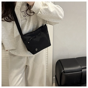 Detail of a black nylon crossbody bag with adjustable strap shown on a model