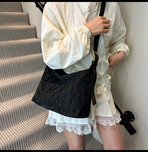 Detail of black pleated crossbody bag with adjustable strap and gold buckle hardware
