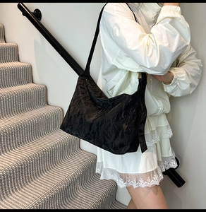 Detail of black pleated shoulder bag featuring cloud texture and golden metal buckle