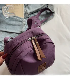 Détail d'un sac bandoulière en nylon violet avec double fermeture éclair et tirettes en cuir