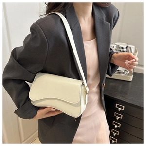 Chic cream leather underarm bag featuring a wave flap design worn by a model in a suit