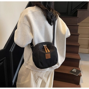 Détail d'un sac bandoulière en nylon noir avec tirettes et logo en cuir marron