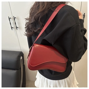 Detail of a dark red patent leather shoulder bag worn by a model in a minimalist room