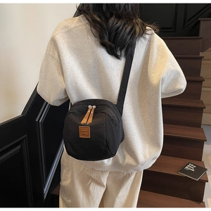 Détail d'un sac bandoulière en nylon noir avec double fermeture éclair et logo en cuir
