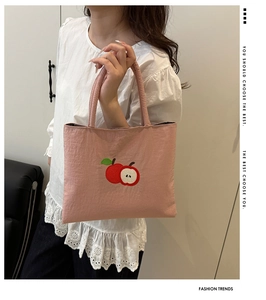 Detail of pink canvas tote bag featuring delicate red apple embroidery and pleated texture