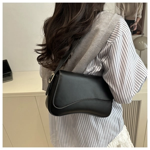 Close-up of black matte leather saddle bag with flap closure and adjustable gold buckle strap