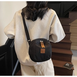 Gros plan sur le sac bandoulière en nylon noir avec détails en cuir et double fermeture
