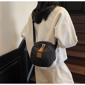 Détail du sac de poitrine en nylon noir avec logo en cuir marron porté par un modèle