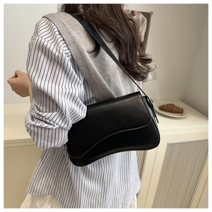 Detailed view of black leather shoulder bag with unique wavy asymmetrical flap design