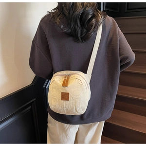 Détail du sac bandoulière plissé beige avec étiquette en cuir et bandoulière large