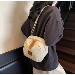 Détail macro du sac bandoulière en nylon crème avec double fermeture éclair et logo en cuir