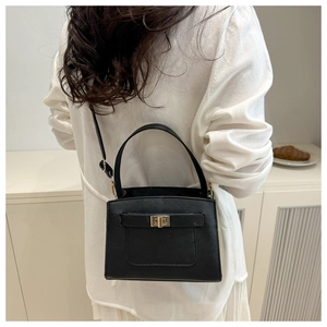 Detailed view of black Saffiano leather handbag with gold turn-lock worn by a model