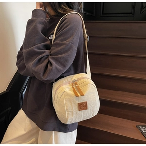 Gros plan du sac bandoulière en nylon beige avec plusieurs fermetures éclair en cuir