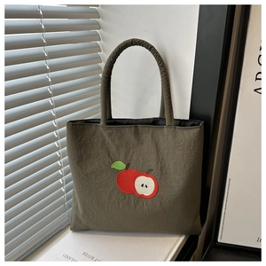 Detail of embroidered apple pattern on dark green nylon bag with soft padded handles