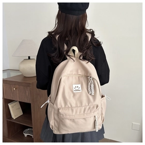 Detail of a beige canvas backpack featuring a fashion woven zipper pull and a smiley patch