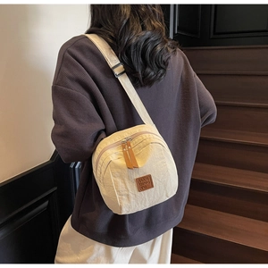Détail du sac à bandoulière beige avec tirettes en cuir marron et étiquette de logo chic