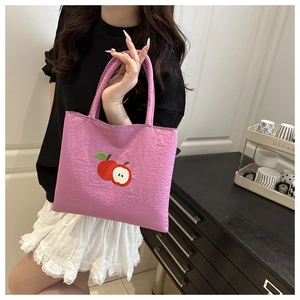 Pink textured handbag detail featuring red apple embroidery and double handle style