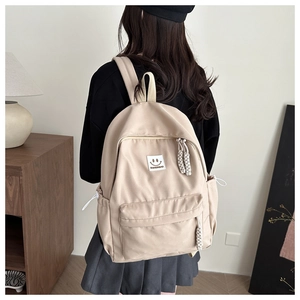 Detail of beige nylon backpack featuring a smiley patch and woven rope zipper pull