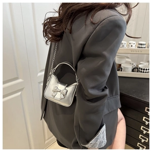 Detail of silver mini bow handbag with metal chain strap and curved handle design