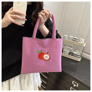 Detail of purple-pink crinkle fabric tote bag featuring a red apple embroidery