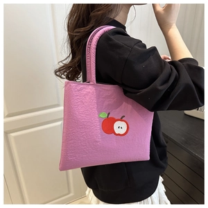 Detail of pink tote bag showing intricate red apple embroidery and soft fabric texture