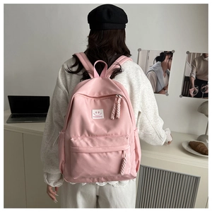 Close-up of pink canvas backpack featuring a woven zipper pull and a white smiley face patch