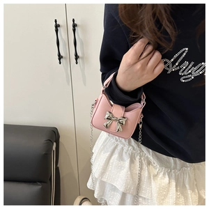 Close-up of a mini pink crossbody bag with a silver bow and metal chain strap on a model