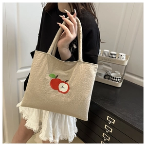 Detail of cute apple embroidery on cream nylon tote bag held by a person