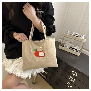 Macro shot of minimalist beige canvas handbag featuring red apple embroidery and top handles