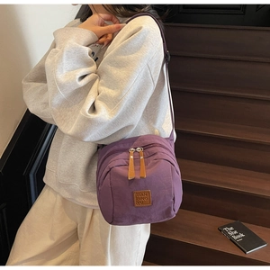 Détail d'un sac bandoulière en nylon violet avec zips multicouches et logo en cuir chic