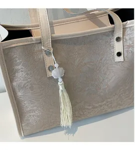 Detail of beige tote bag with embossed floral texture, silver rivets, and lotus tassel