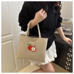 Detail of beige nylon tote bag featuring red apple embroidery and double handles