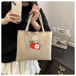 Detail of off-white tote bag featuring red apple embroidery and crinkle texture fabric