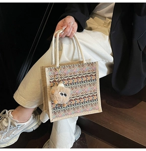 Ethnic woven tote bag with colorful patterns and cute pom-pom charm on wooden background