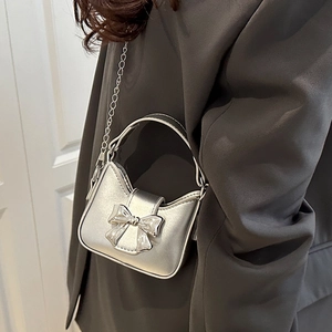 Chic silver bow mini handbag with metal chain strap worn over a dark grey blazer