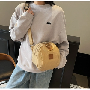 Détail du sac bandoulière en nylon beige avec doubles fermetures éclair et patch logo en cuir