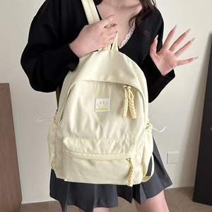 Minimalist cream nylon backpack featuring a yellow smiley face patch and rope zipper pulls