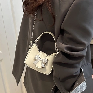 Mini cream leather crossbody bag with silver bow accent and chain strap on grey blazer