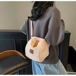 Vue latérale du sac bandoulière rose clair avec fermetures en cuir marron et logo discret