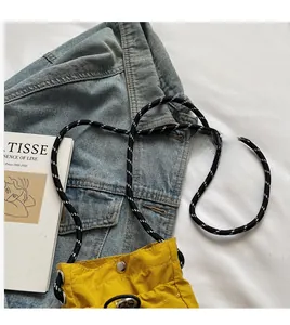 Detail of a bright yellow nylon crossbody bag with striped rope strap and silver metal button