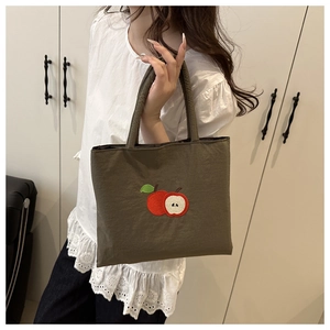 Detail of olive green canvas tote bag featuring embroidered red apple design on fabric