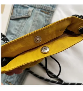 Detail of yellow nylon crossbody bag featuring a silver metal snap button and woven strap
