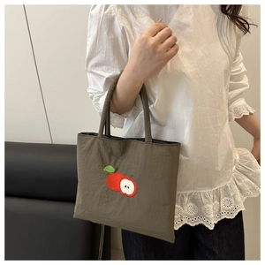 Close-up of apple embroidery on olive green nylon tote bag held by a model
