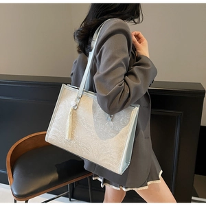 Detail of light blue tote bag featuring white floral jacquard and elegant tassel charm
