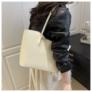 Close-up of cream woven tote bag with shoulder strap worn by a model in a stylish outfit